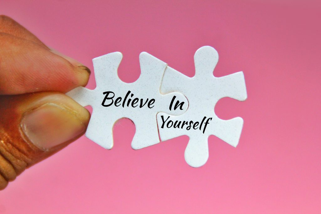 Hand connecting two puzzle pieces that read "believe in yourself," symbolizing the mindset behind becoming your best self